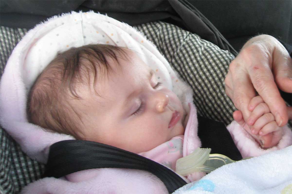 Baby in a car seat holding a person's hand