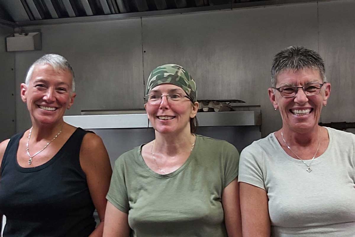 Three women smiling in a restaurant kitchen.