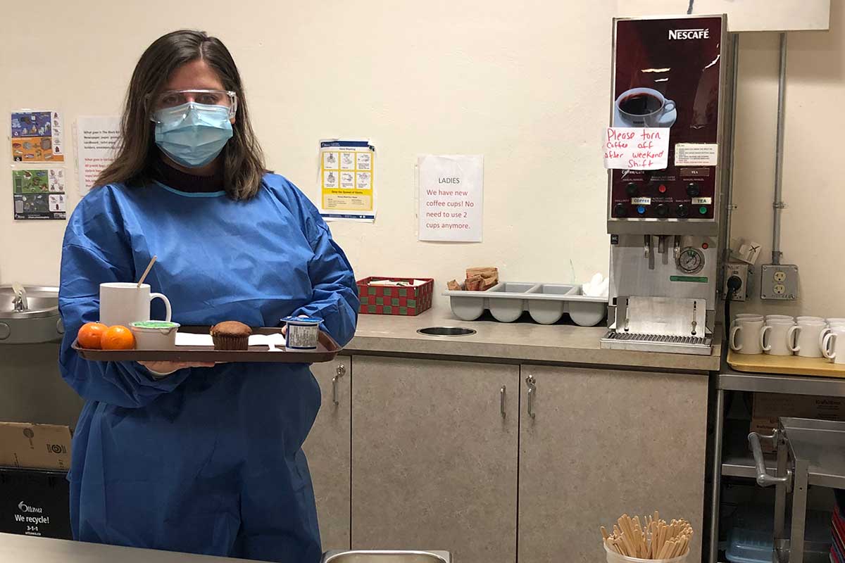 Woman in PPE holding a serving tray with refershments