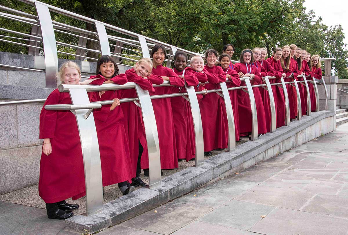 Girls choir members pose in a row wearing red robes