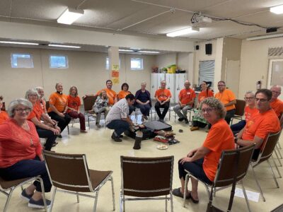 People wearing orange shirts sitting in a large circle around an Indigenous man