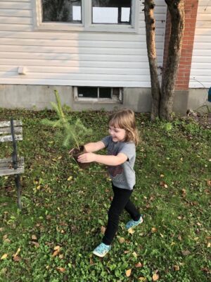 A young girl runs with a seedling tree. 