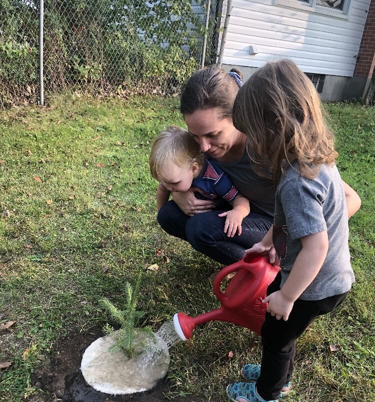 The Rev. Gillian Hoyer holds her son Thomas while her daughter Lily waters a seedling.