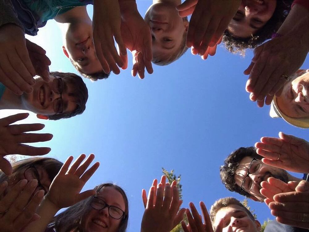Faces and hands of youth in a circle with blue sky background
