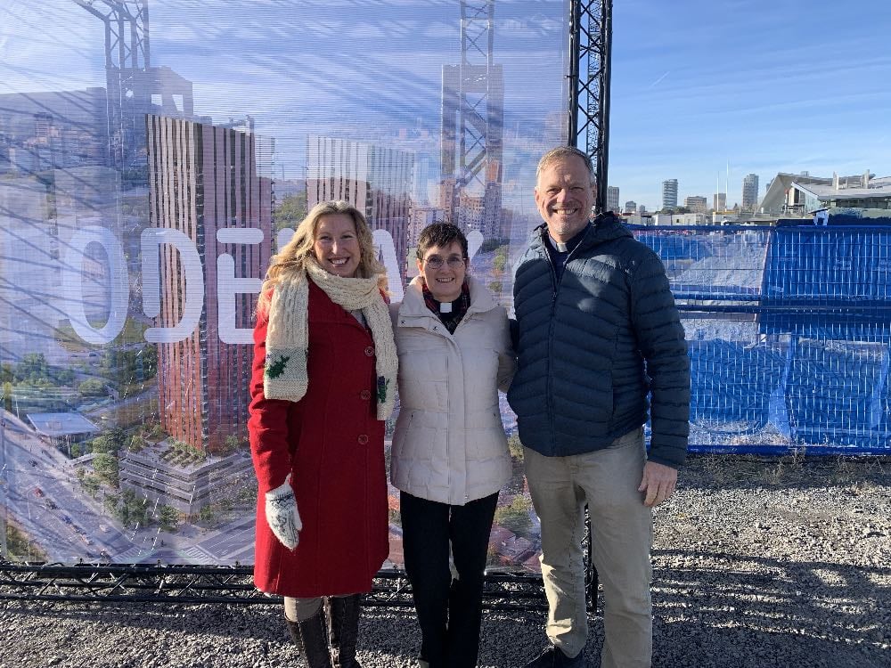 Three people stand in front of the Odenak sign at the construction site