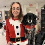 A woman in a Christmas sweater holds a dog also dressed in red.