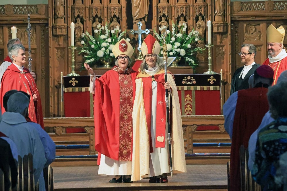 Archbishop Anne Germond and Bishop Kathryn Otley stand in front of the altar at Christ Church Cathedral Ottawa resplendent in red and gold robes and mitres.