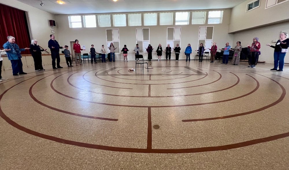 People stand on the edge of the labyrinth on the floor in the hall of Julian of Norwich Anglican Church.