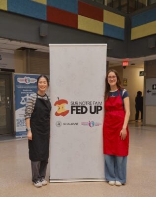 Two young women stand beside a vertical banner that says Fed Up.