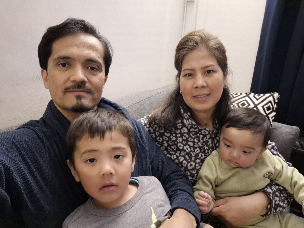 A husband and wife from Afghanistan sit on a couch holding their two young boys.