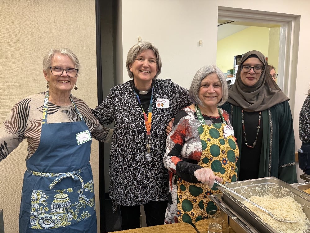 Four smiling women stand behind the buffet table, momentarily pausing from serving the meal.