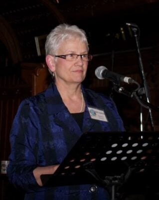 A silver-haired woman speaks into a microphone
