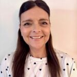 Michele Allen with long dark hair wearing a polka-dot shirt with hearts and a cross necklace.