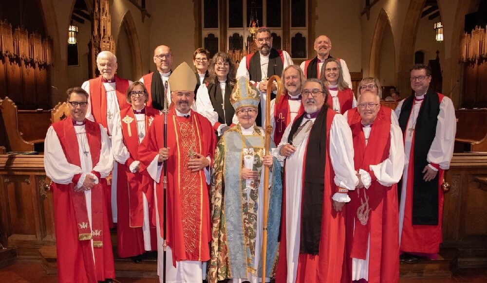 Bishop Jennifer Gosse-Vingerhoeds poses with the Primate and other bishops for a photo after her consecration. Eveyone is wearing red and white robes.