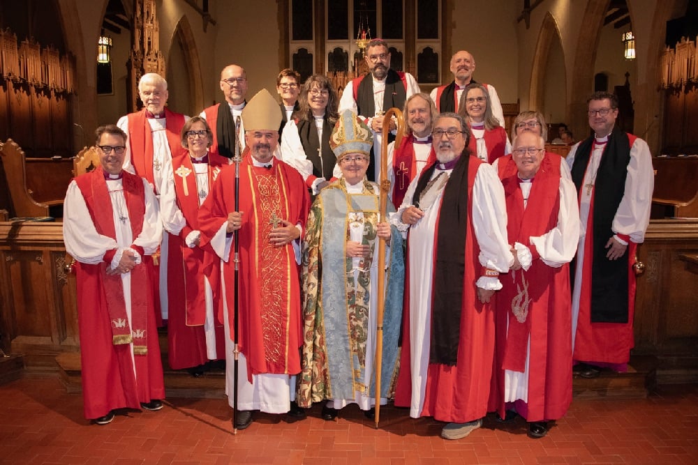 Bishop Jennifer Gosse-Vingerhoeds poses with the Primate and other bishops for a photo after her consecration. Eveyone is wearing red and white robes.